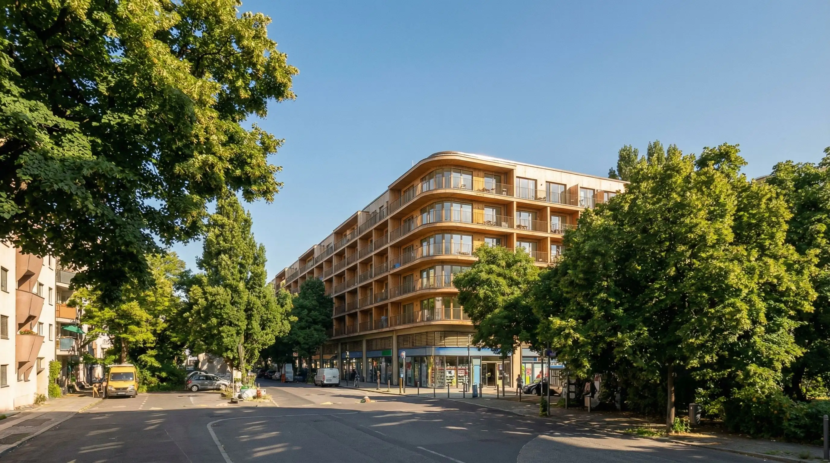 Straßenperspektive mit Wohnfassaden, Balkonen, Erdgeschossaktivität und Bäumen.